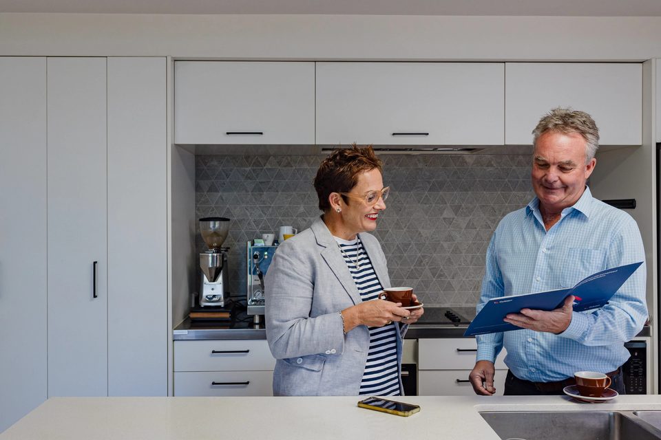 A rental manager and a property owner talking over a blue folder in a kitchen.