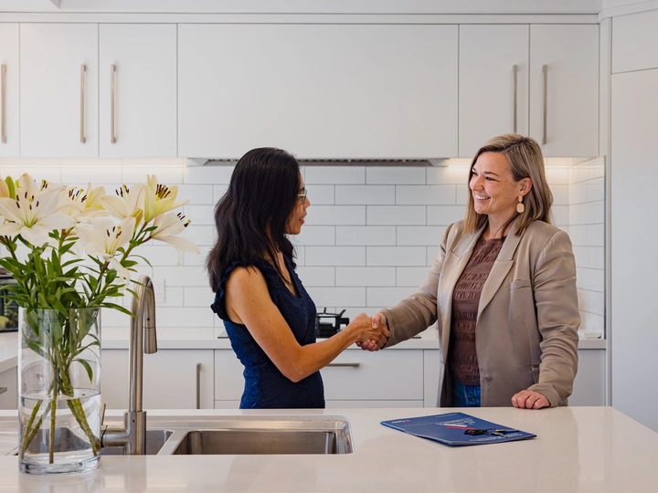 Two women shaking hands across a white kitchen bench in a Pukeko rental management meeting.